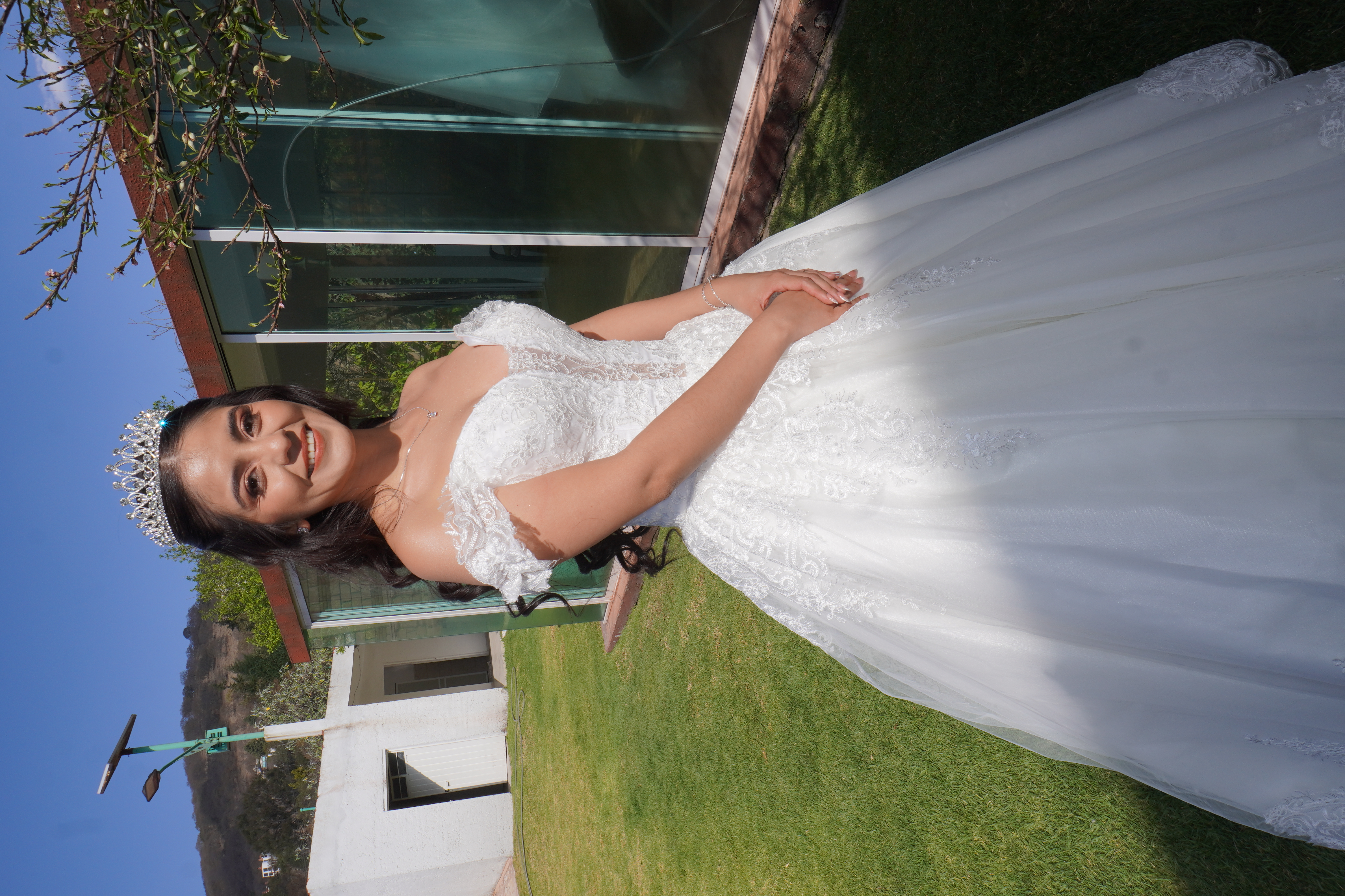 Novia sonriendo con corona y vestido completo en el jardin