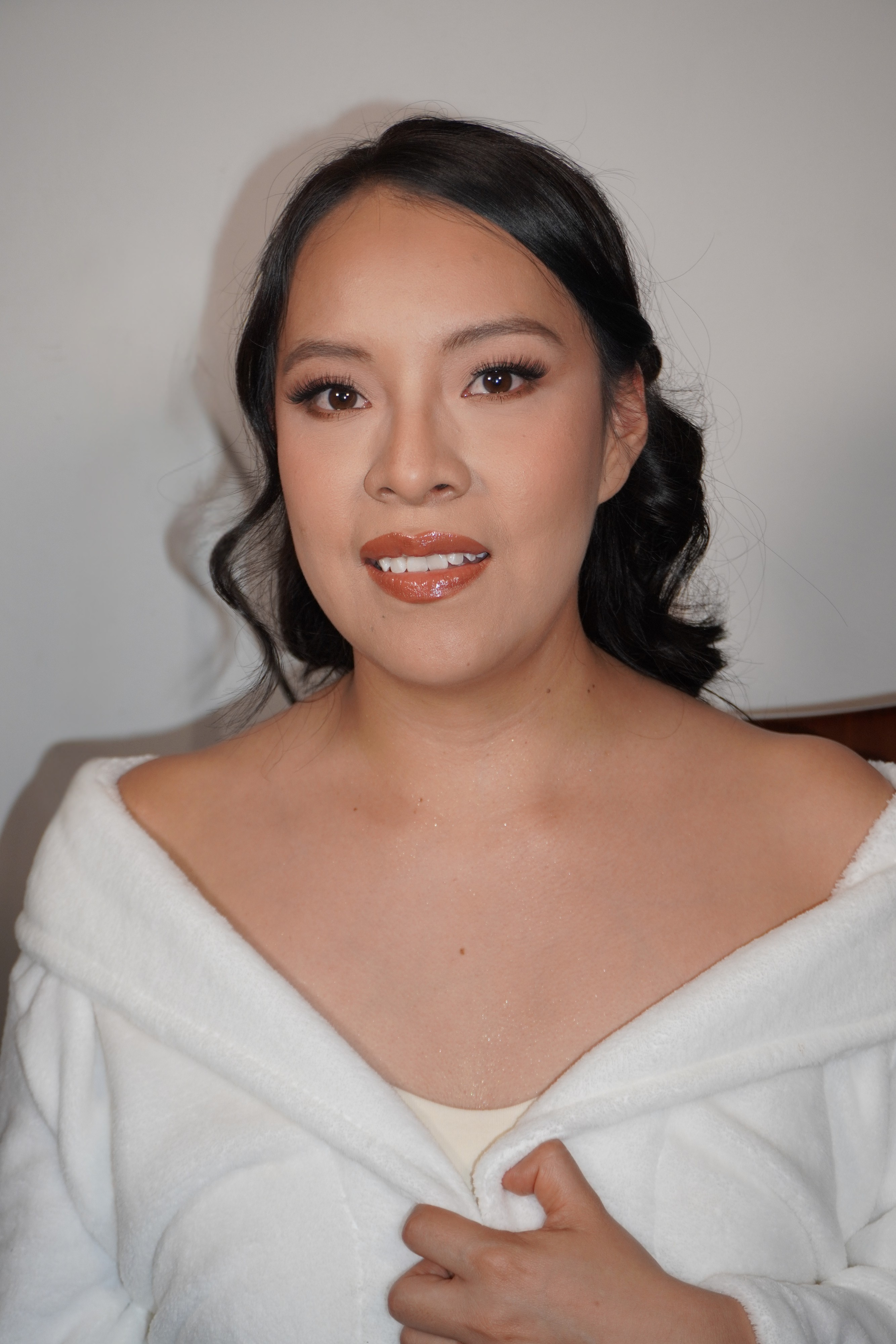Novia en bata blanca con maquillaje terminado antes de vestirse