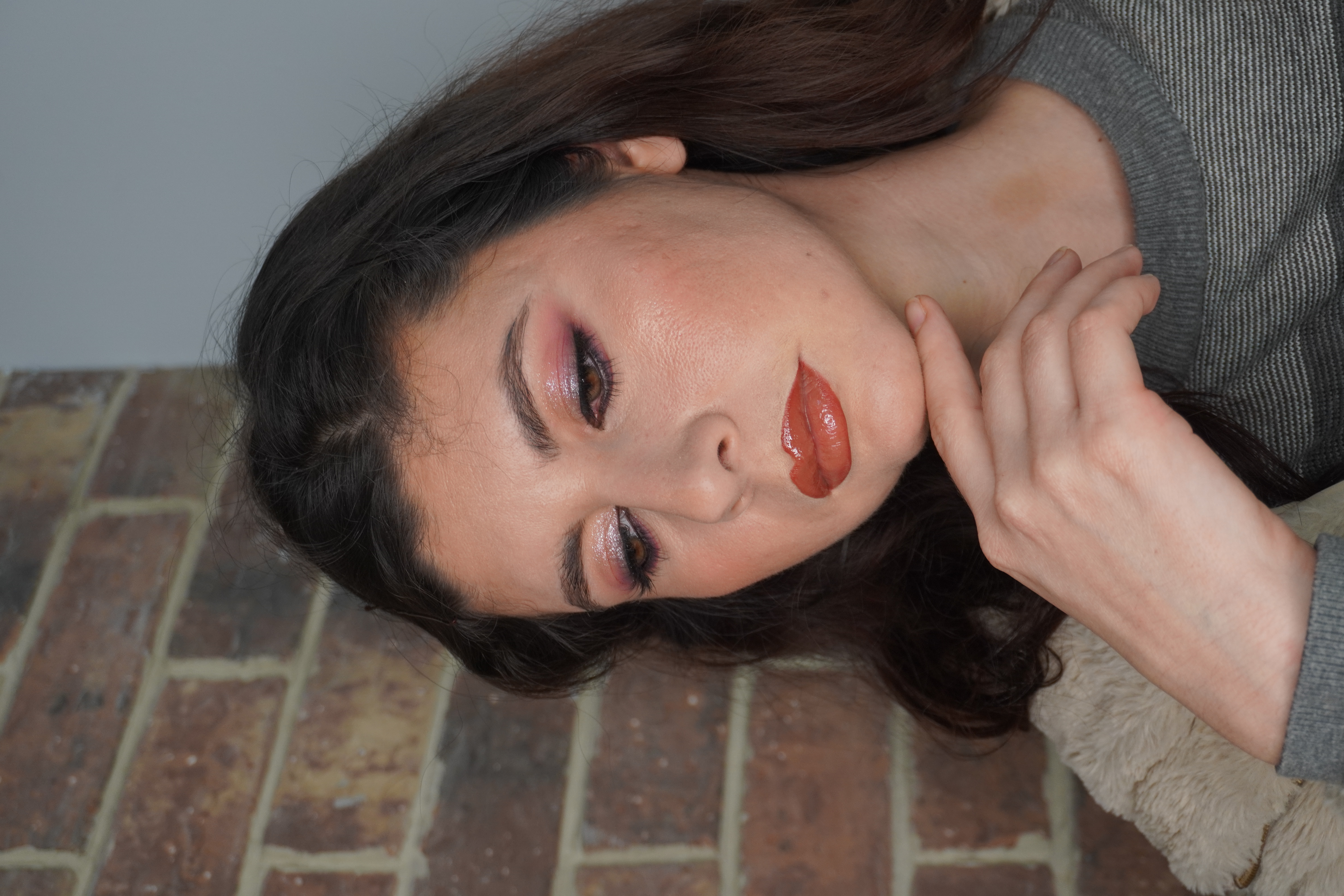 Retrato con sombra morada y labios naranjas sobre pared de ladrillo